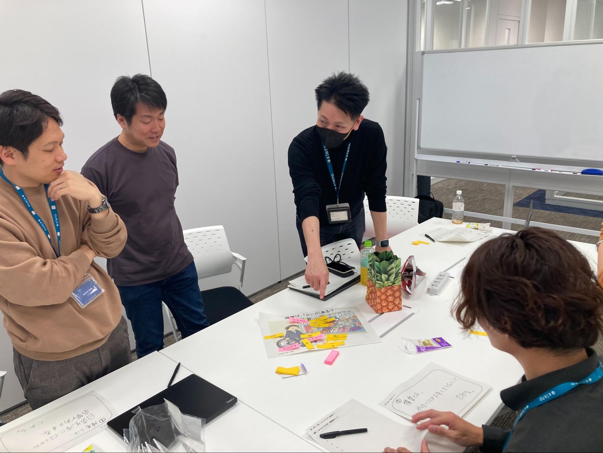 3名の参加者が机を囲み、手元の資料を指差しながら真剣に、かつ前向きな様子で話し合っている後ろ姿。