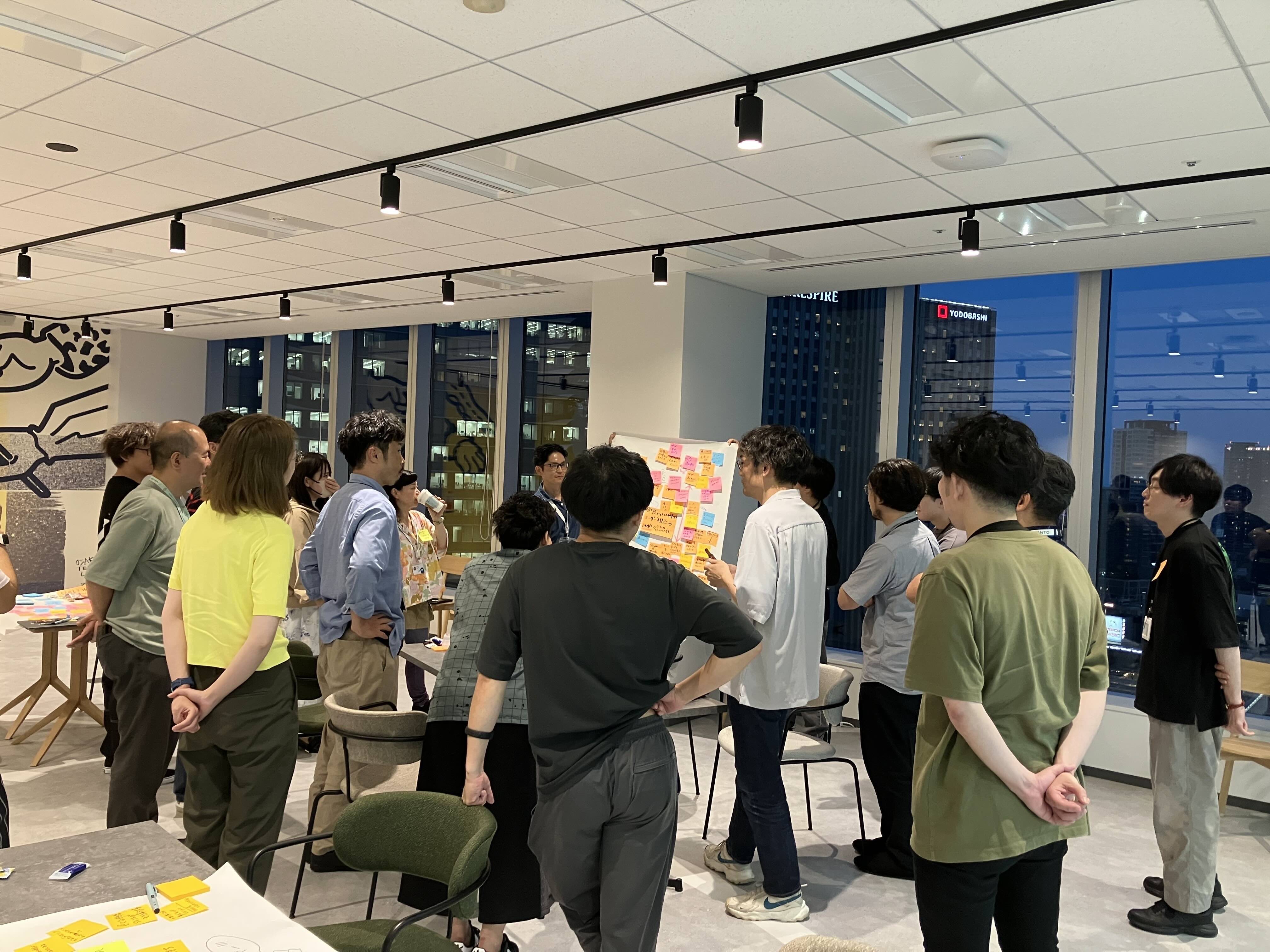 Techラウンドテーブル開催の様子：複数の男女が付箋一覧を囲み意見を交わしている写真
